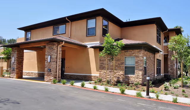 Two-story tan stucco senior living facility with stone accents and a covered entrance