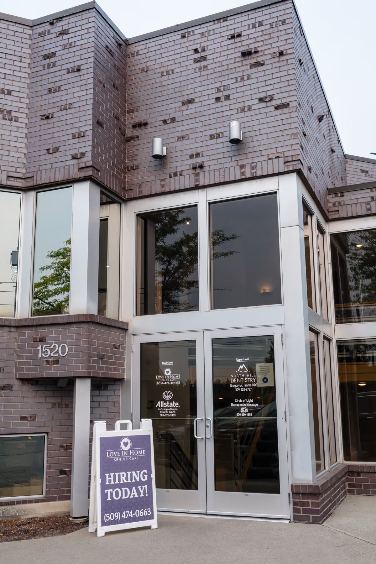 Exterior of Love In Home Senior Care facility with glass doors and a 'Hiring Today' sign.