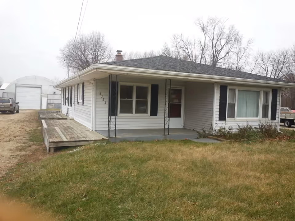 One-story white house with a covered front porch, wooden ramp, and front lawn.