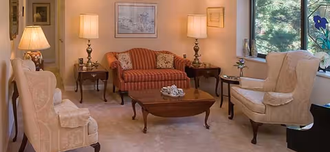 Cozy living room with a striped sofa, two upholstered armchairs, a wooden coffee table, side tables and lamps by a large window.