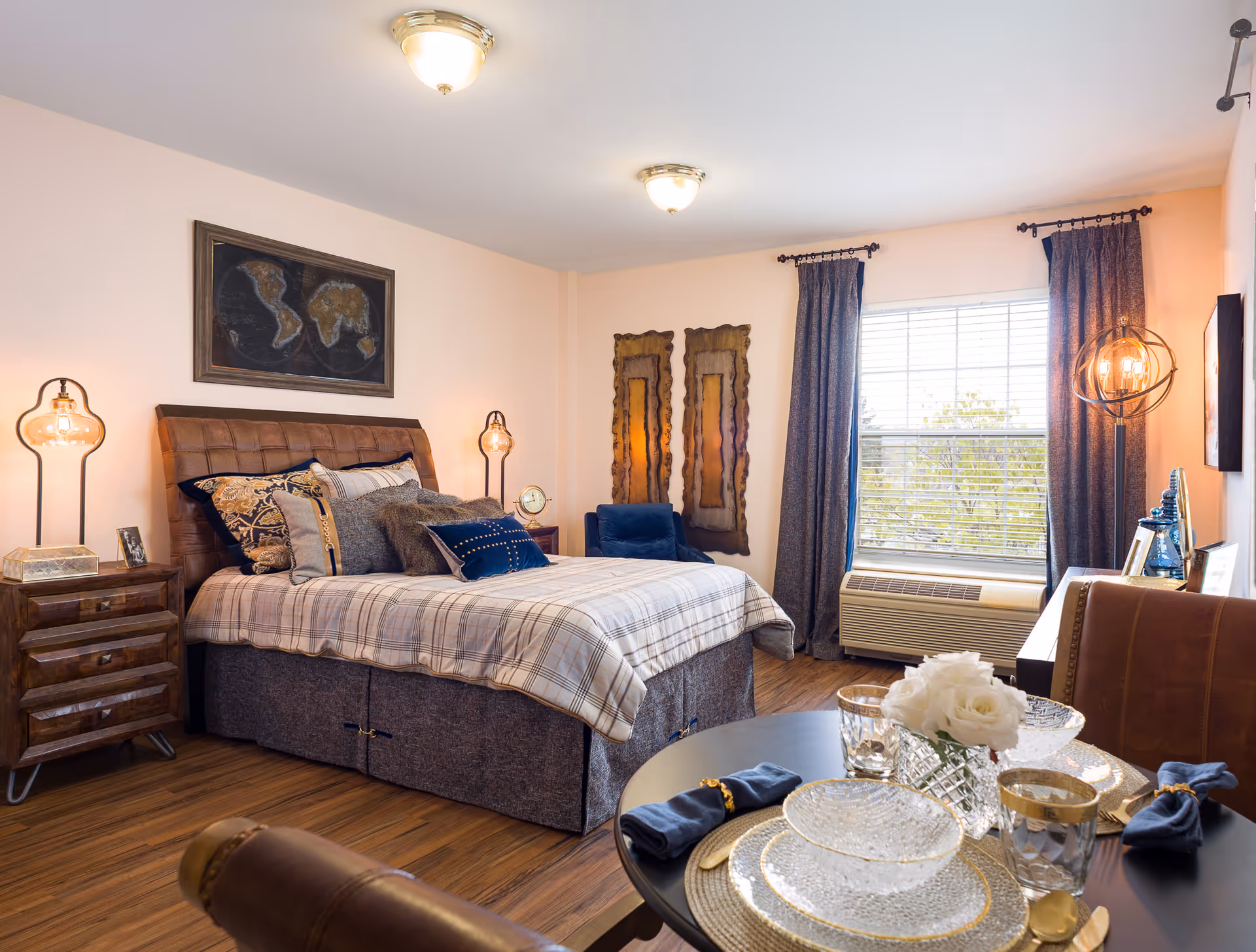 Well-furnished bedroom with bed, nightstands, window, and dining table in warm tones.