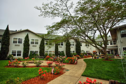 Front exterior of Tanner Spring Assisted Living facility with landscaped gardens and a curved walkway.