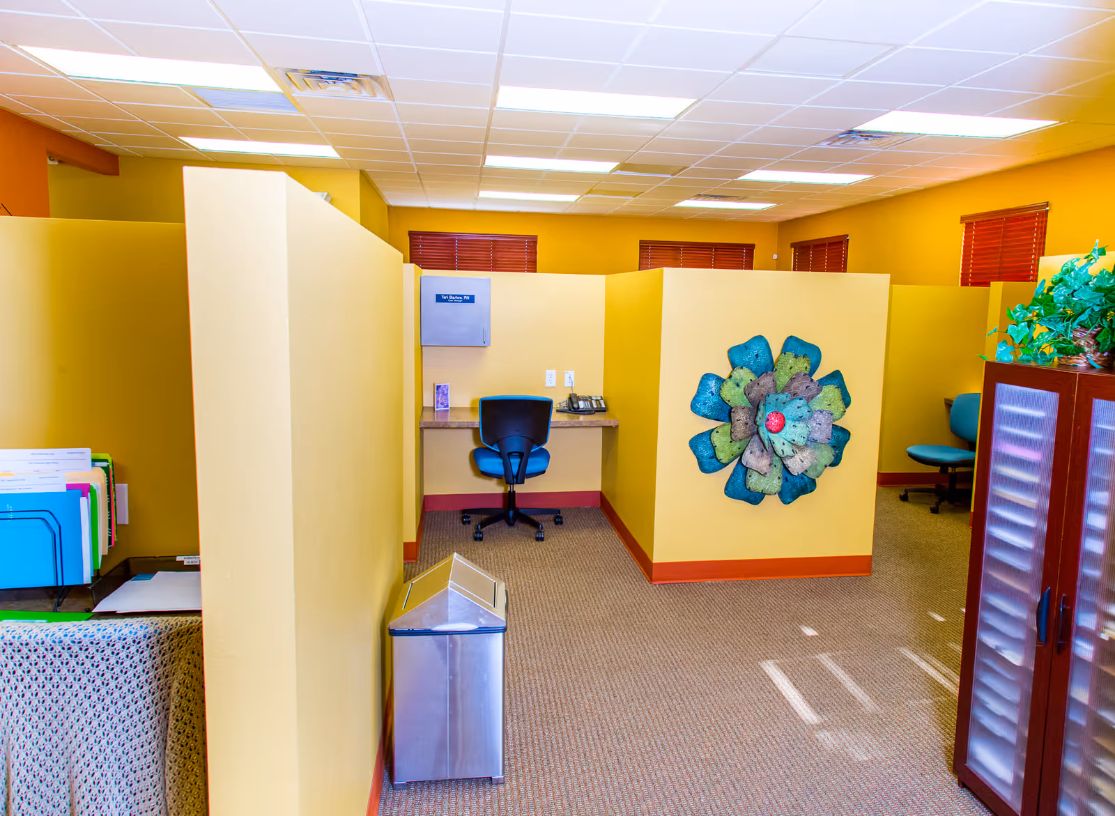 Interior office area with yellow cubicles, a desk chair, and wall art.