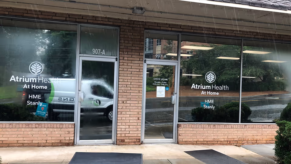 Facade of Atrium Health At Home storefront with glass doors, large windows, and brick exterior.