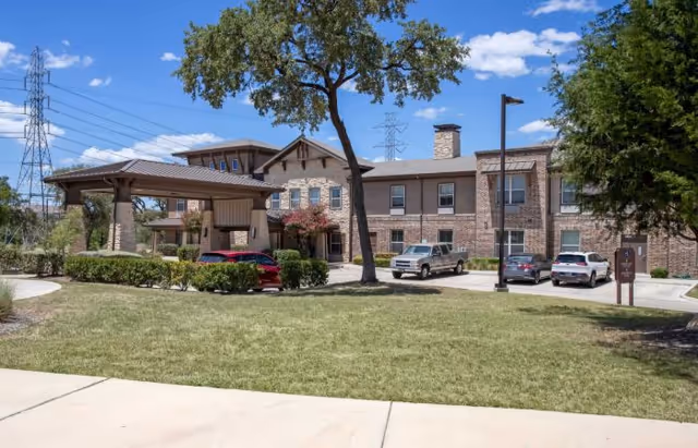 Exterior view of Keowee Square senior living facility with entrance, parked cars, and trees.