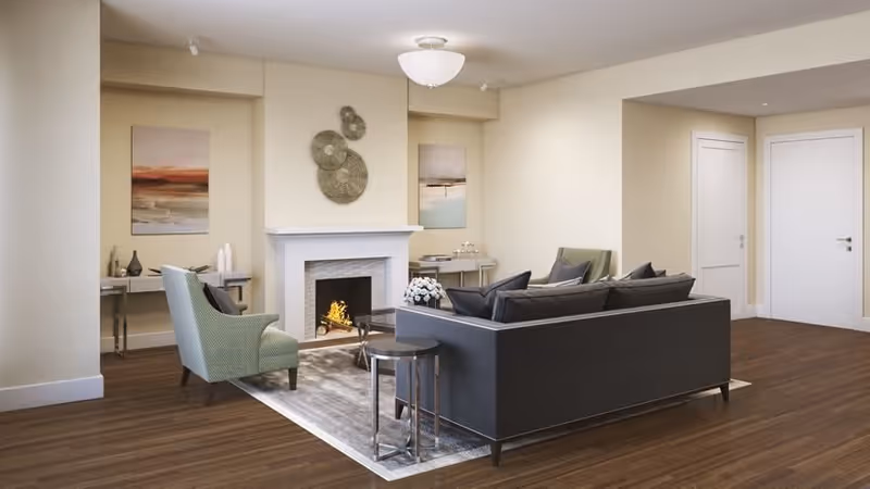 A modern living room with a dark sofa and armchairs arranged around a rug and a lit fireplace beneath wall art.