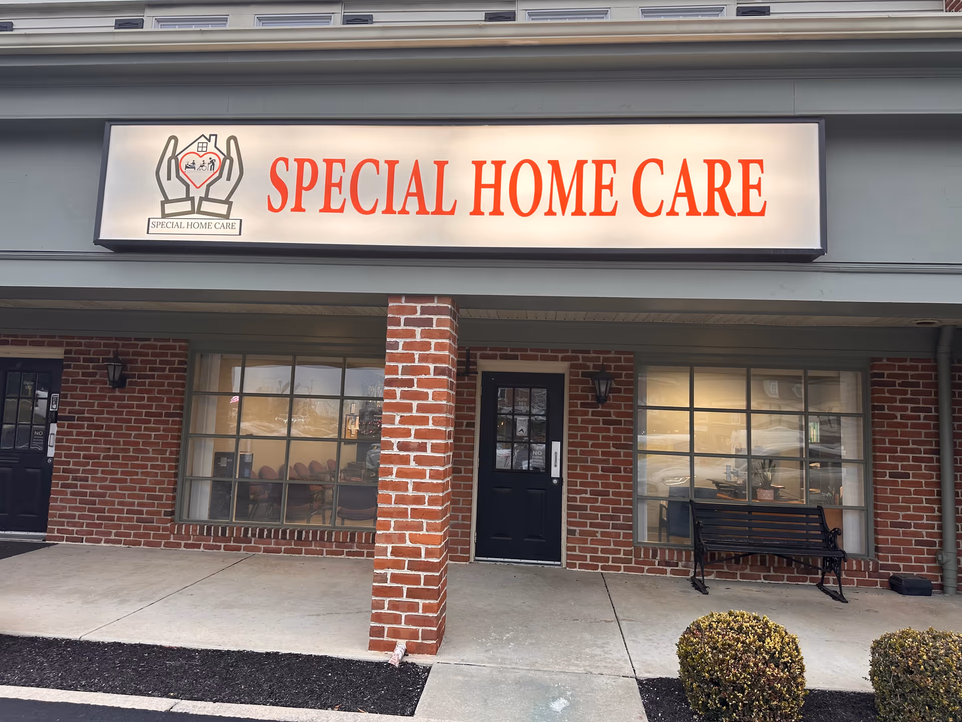 Brick storefront with a large Special Home Care sign and a bench outside.