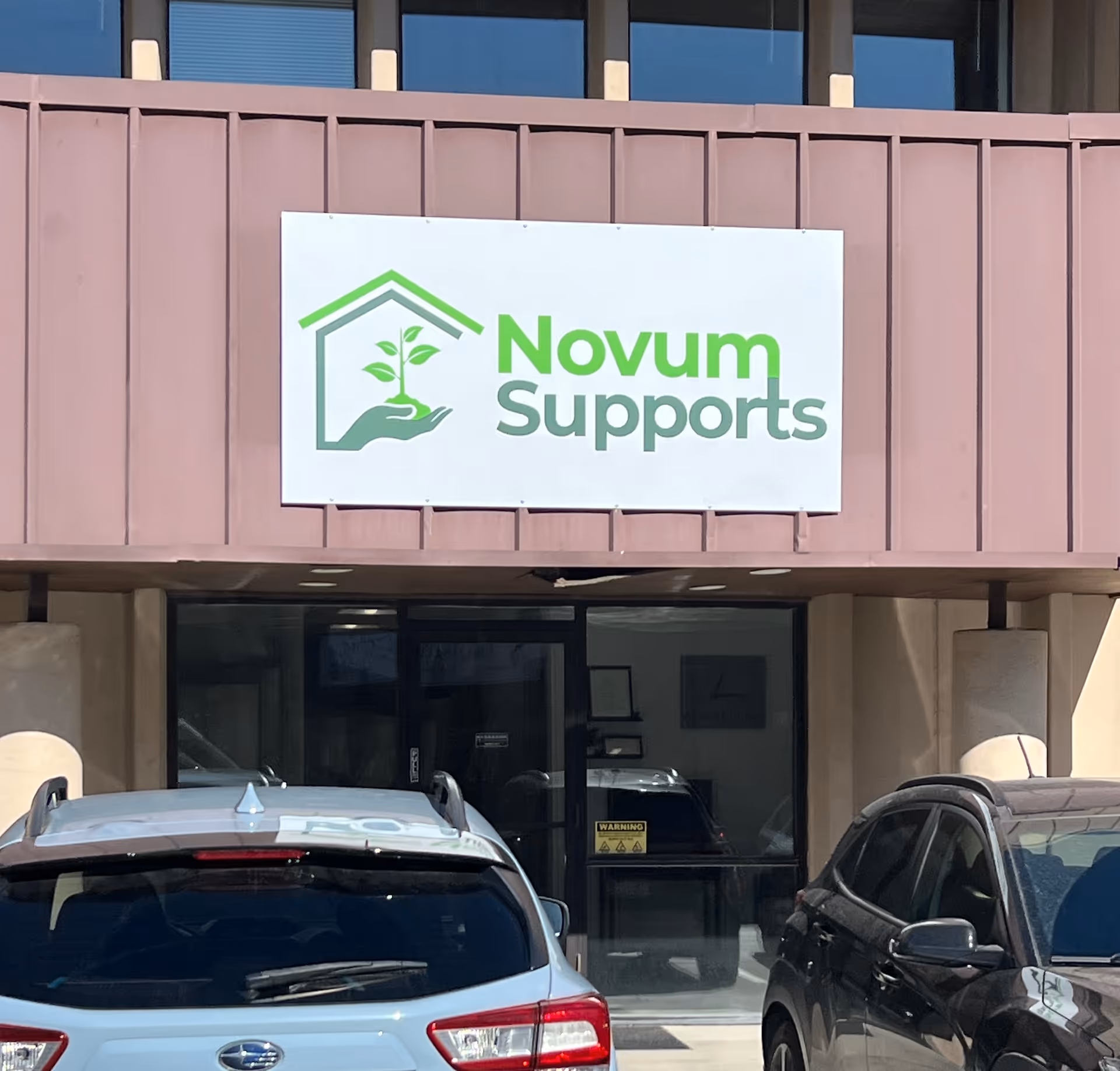 Exterior view of a building with a sign reading Novum Supports and parked cars.