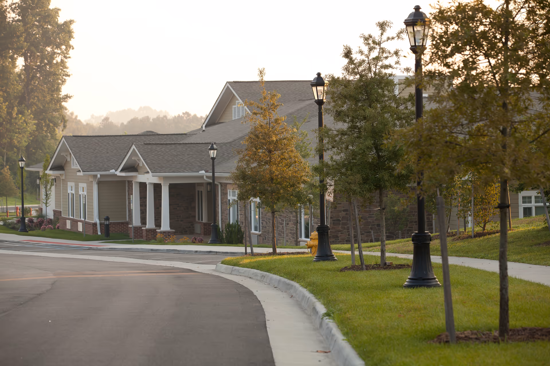 Exterior view of a senior living residence with a stone facade, columns, and a manicured lawn.