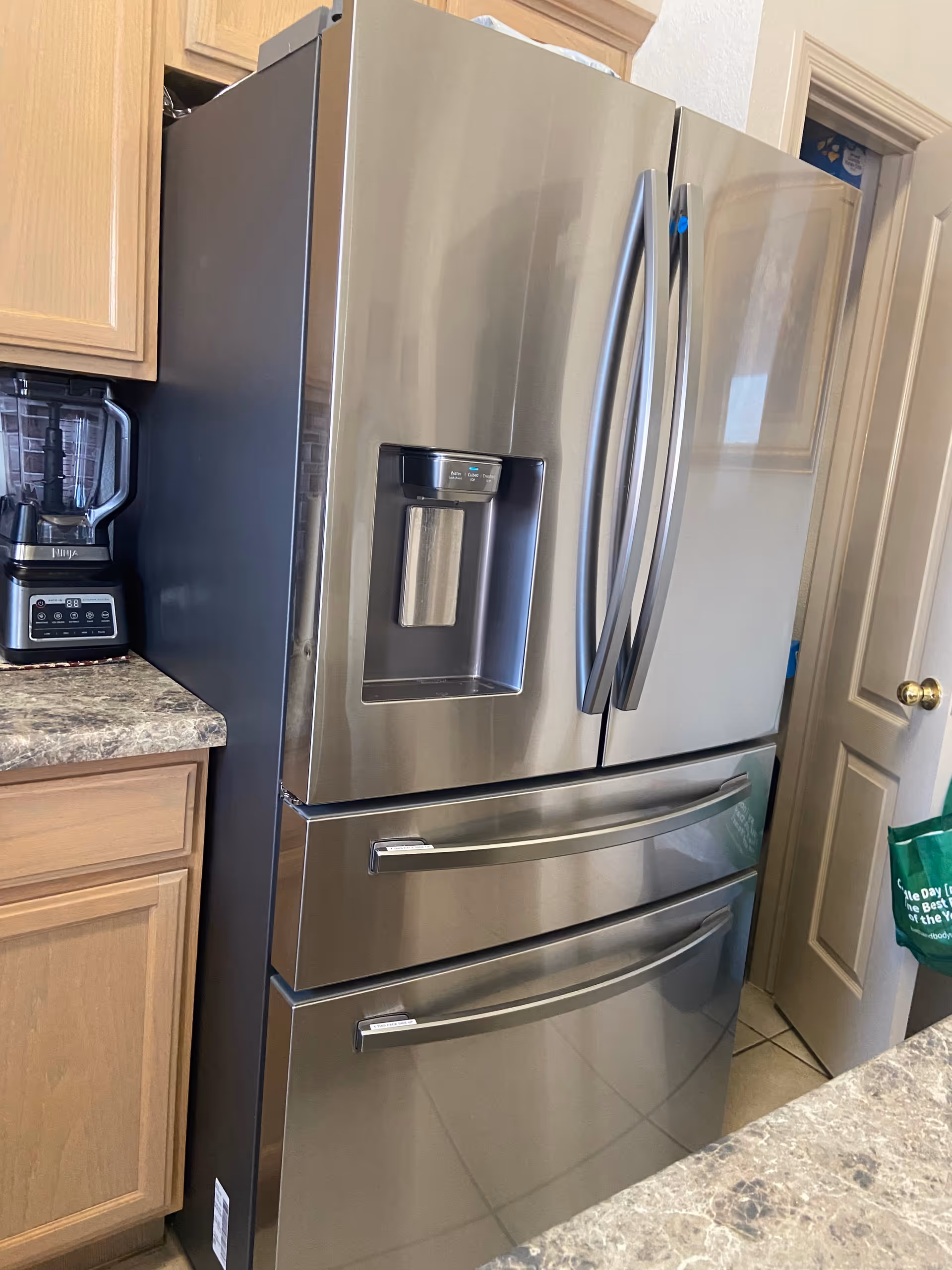 Stainless steel refrigerator with water dispenser in a kitchen, wooden cabinets and countertop.