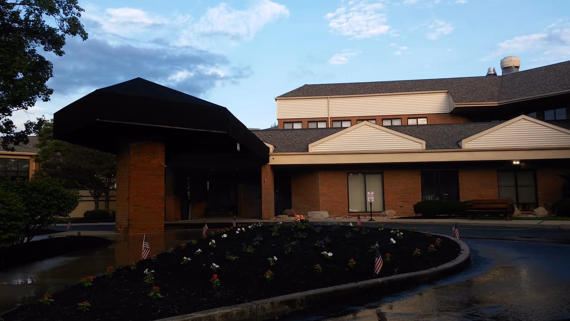 Front exterior of Burlington House Nursing Home featuring brick facade, entry canopy, and flower bed.