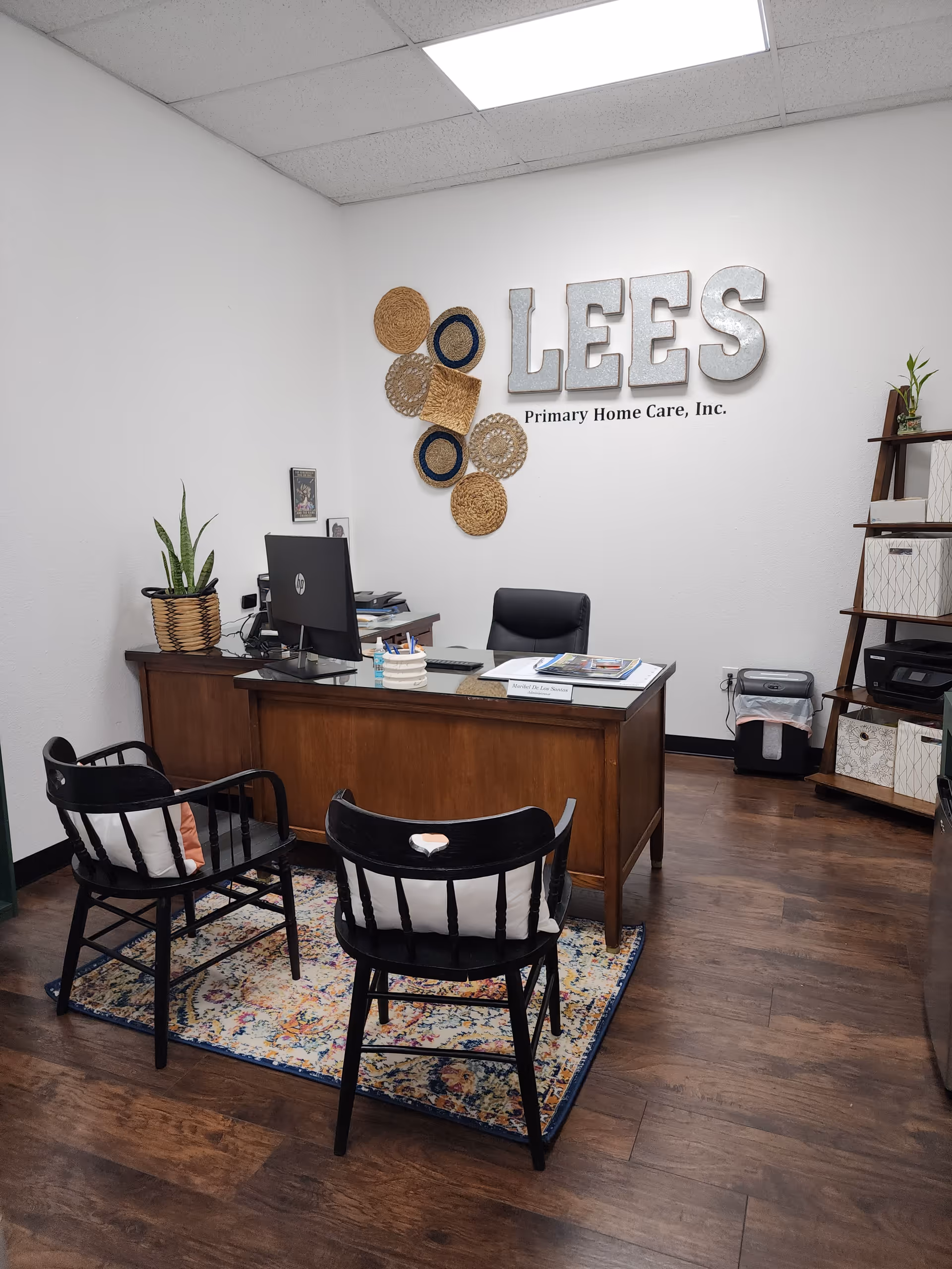 Office reception area with desk, chairs, plant, and Lee's Primary Home Care sign on wall.