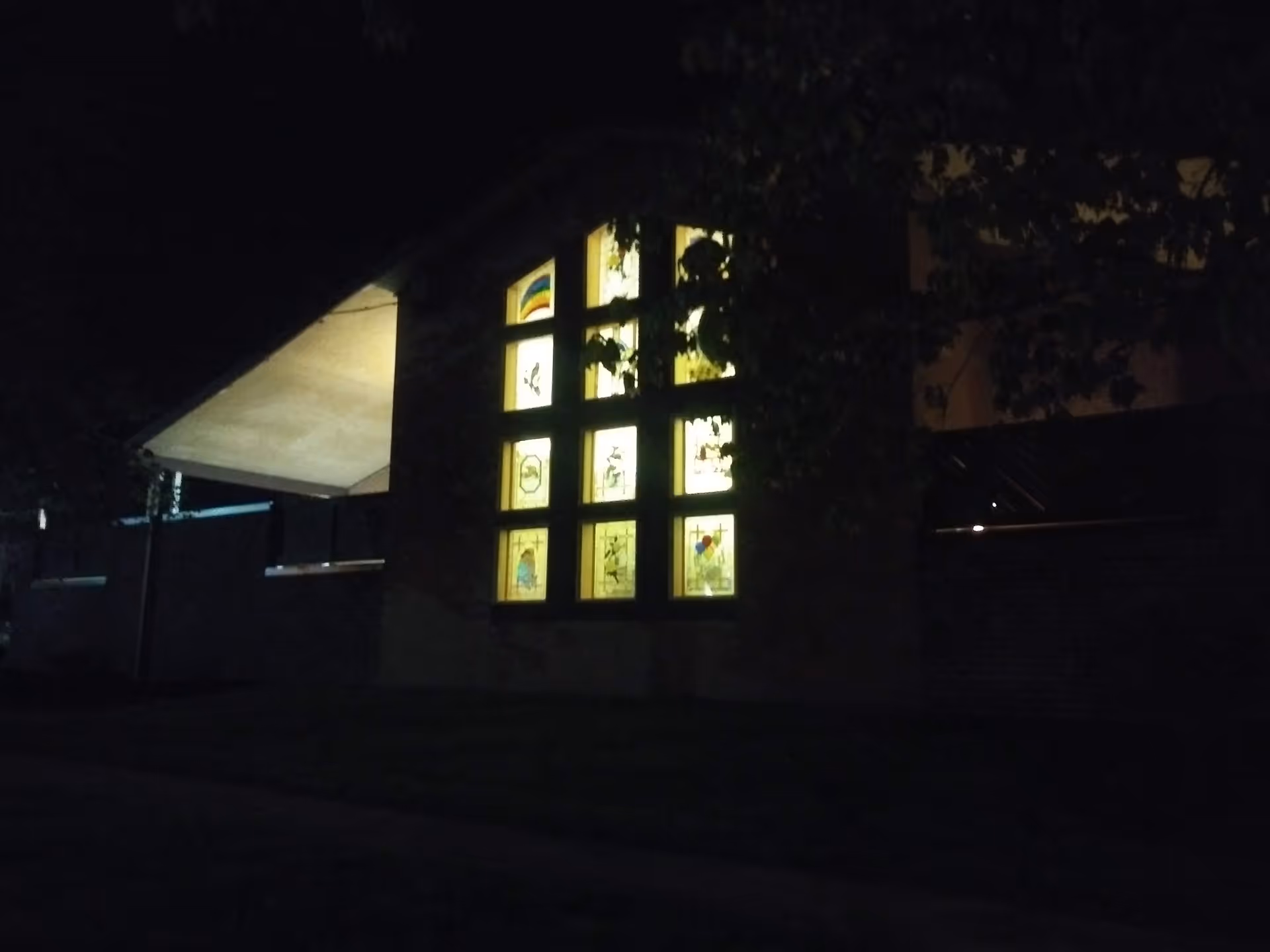 Night exterior of Genesis Hospice Morrison House with illuminated stained-glass windows.