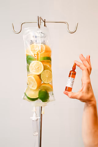 IV bag with citrus fruits hangs from an IV pole; a hand holds a small bottle.
