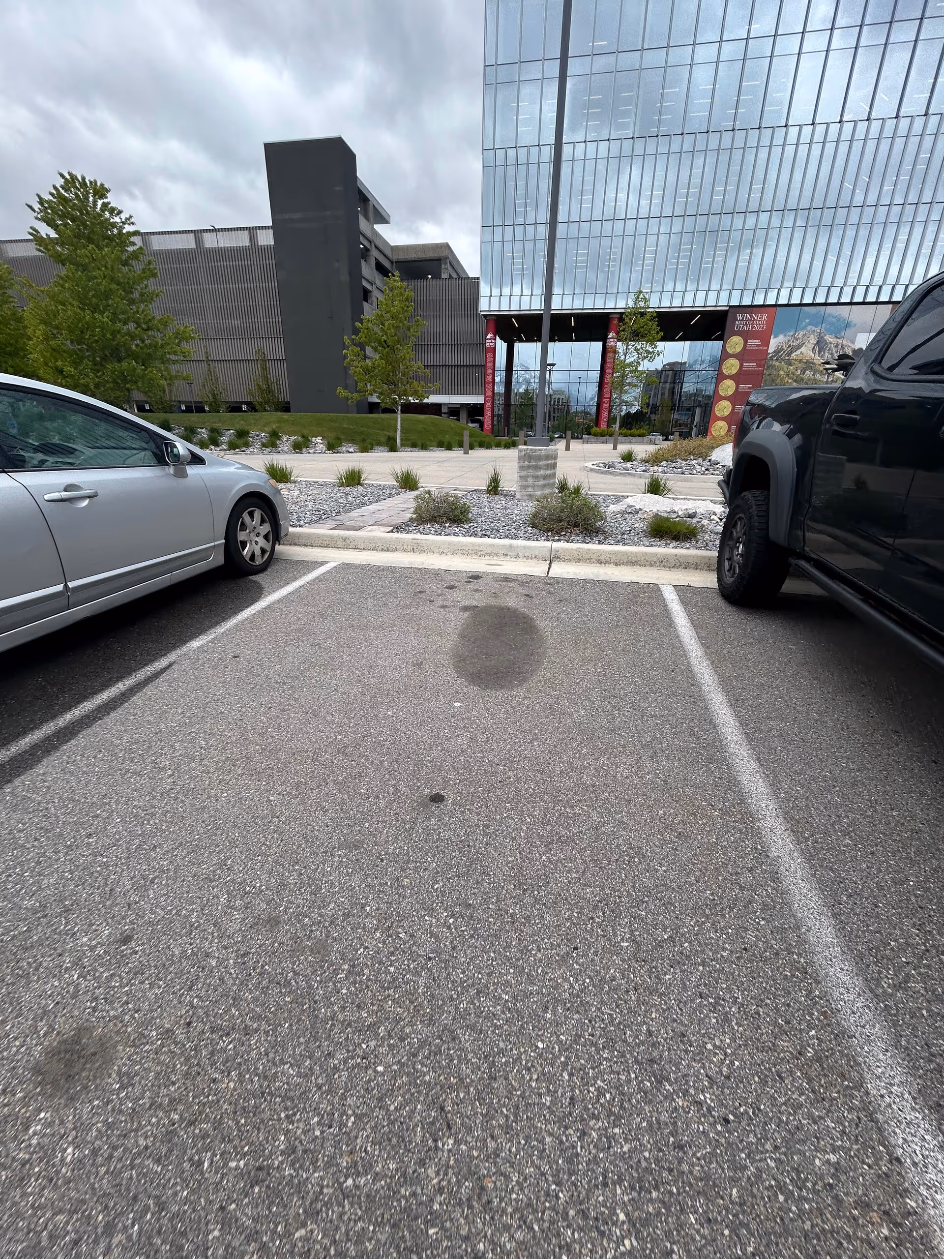 Parking lot in front of a modern glass building with landscaped median and trees.