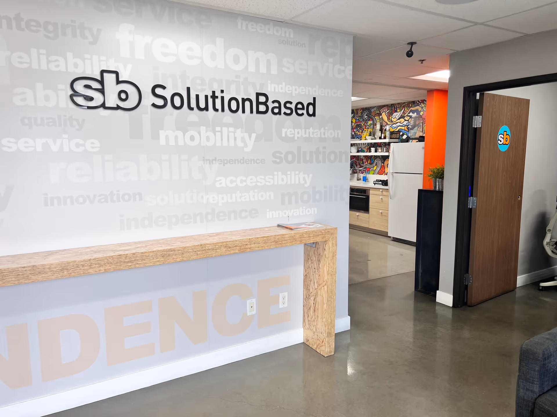 Reception area with branded wall, wooden counter, and visible kitchen in background.