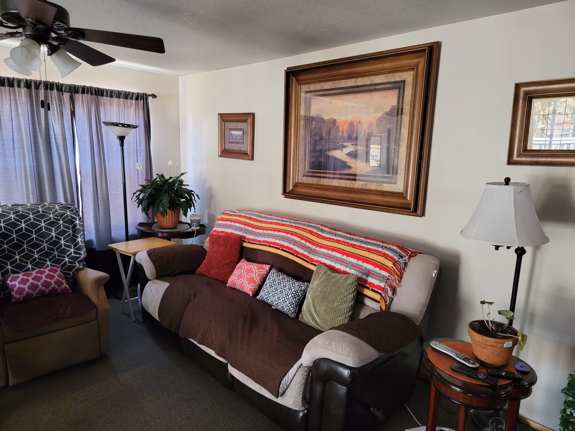 Cozy living room in a senior facility with sofa, armchair, plants, and wall art.