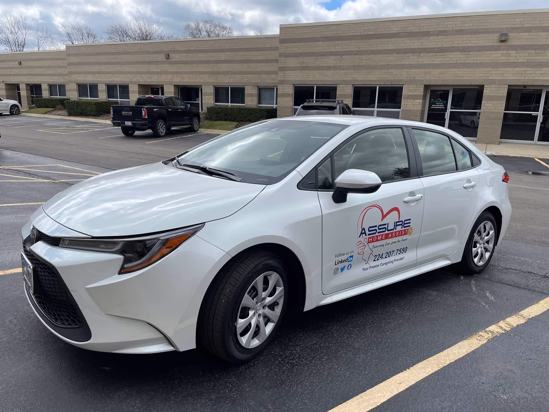 White sedan with Assure Home Assist logo parked outside a beige brick facility