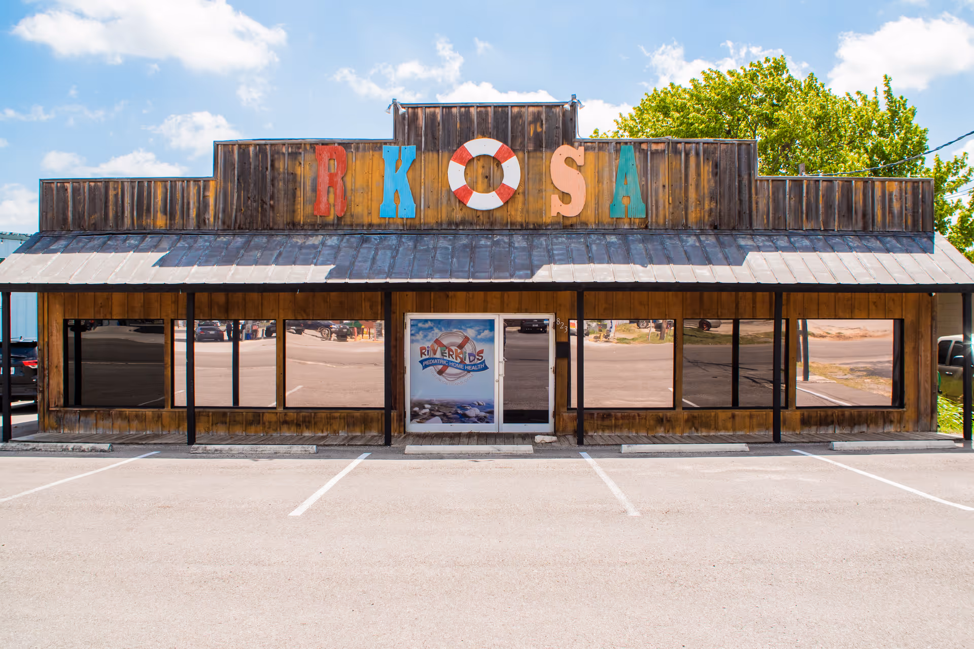 Rustic storefront with large windows and multicolored rooftop sign.