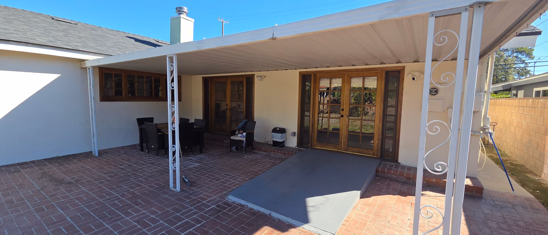 Covered brick patio with outdoor dining table, chairs, French doors, and a ramp leading inside.