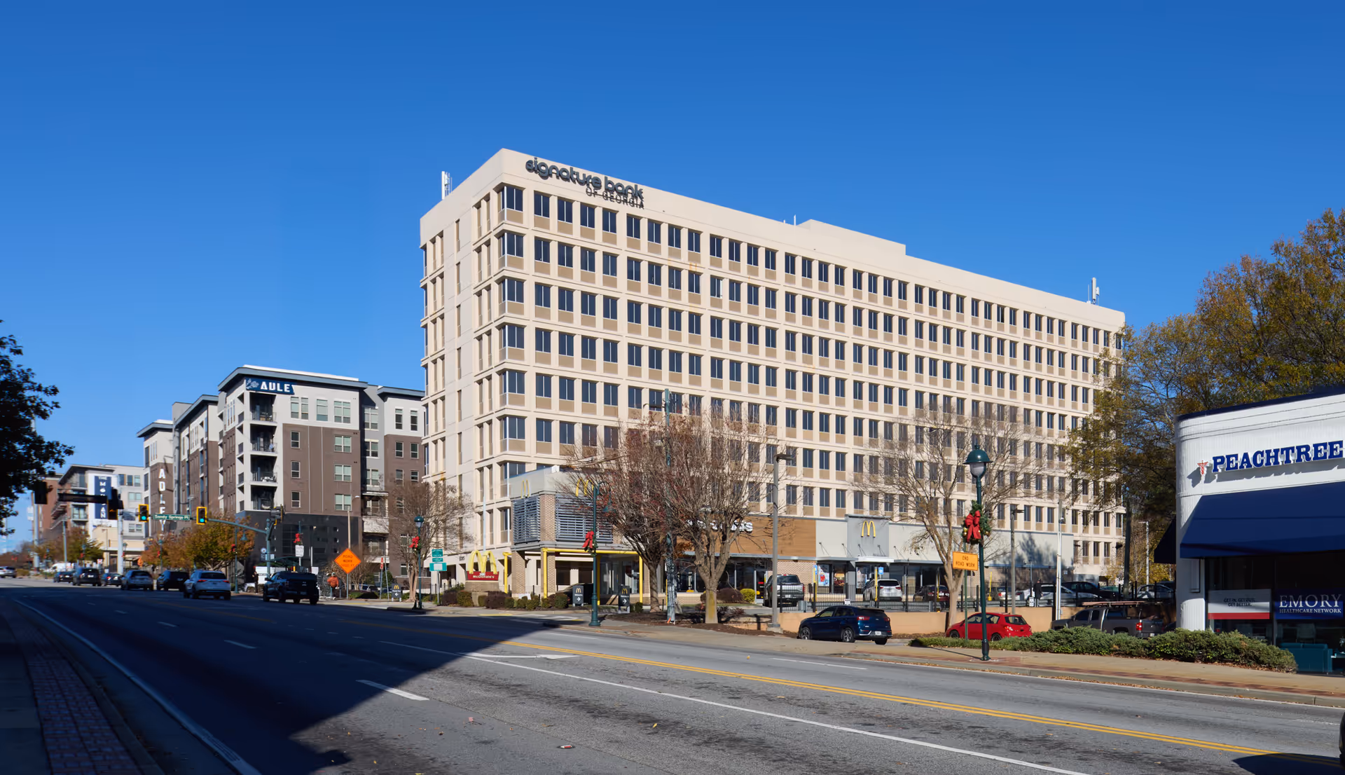 Wide city street view with a large beige multi-story building and storefronts.
