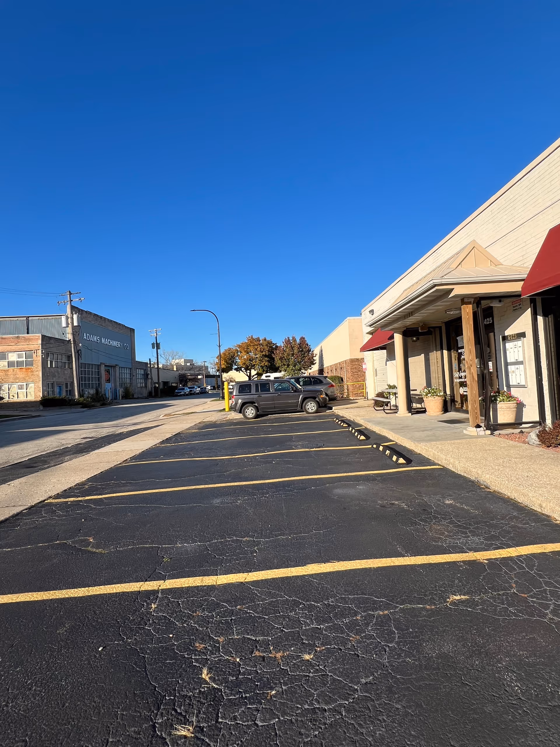 Wide parking lot in front of a beige building with red awnings and blue sky.