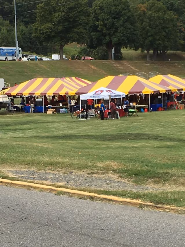 Outdoor scene with yellow and maroon striped tents on a grassy field and people.
