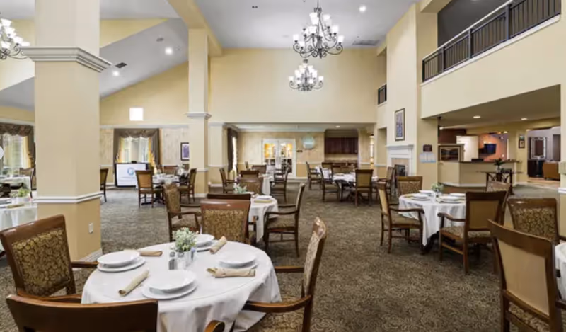 Spacious dining room with round tables set for meals, beige walls, and chandeliers.