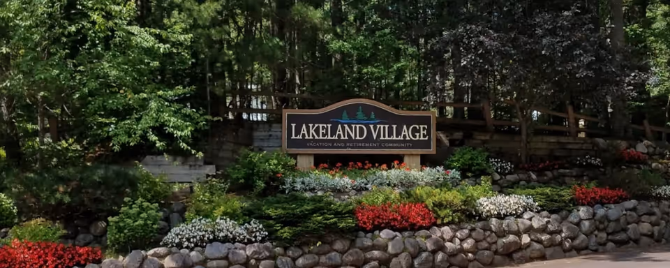 Entrance sign reading Lakeland Village surrounded by a stone wall and colorful landscaping.