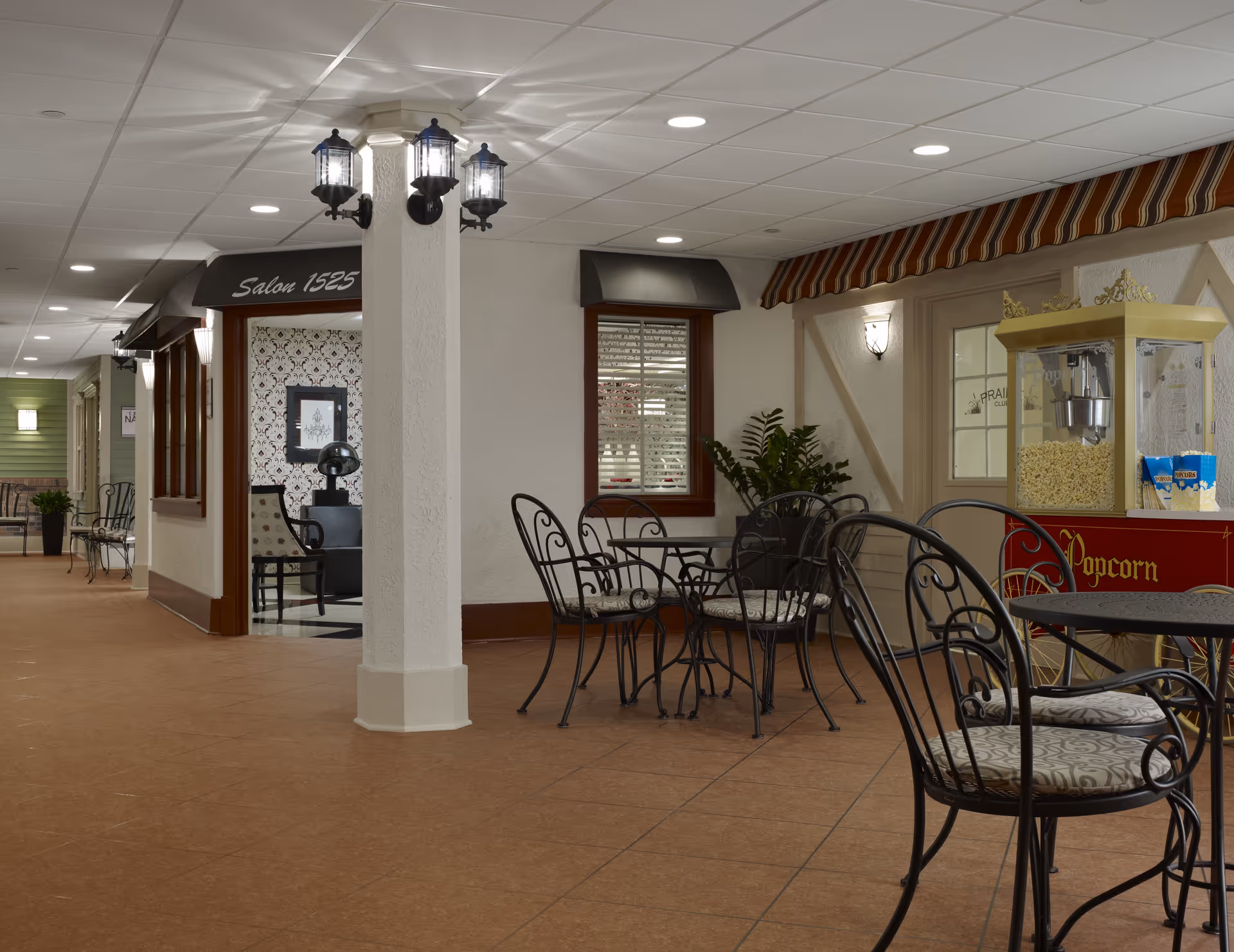 Interior corridor of a senior living facility featuring cafe seating, popcorn machine, and decorative lighting.