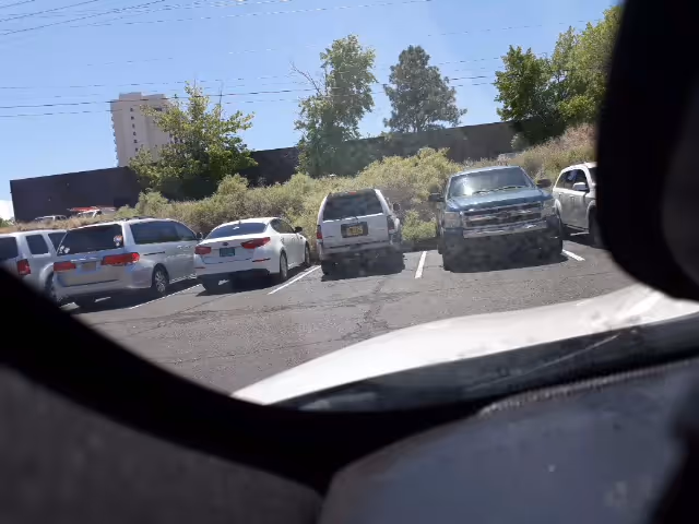 Parking lot of cars outside a building, viewed from inside a vehicle.