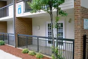 Exterior view of a brick senior living building entrance with railing and greenery.