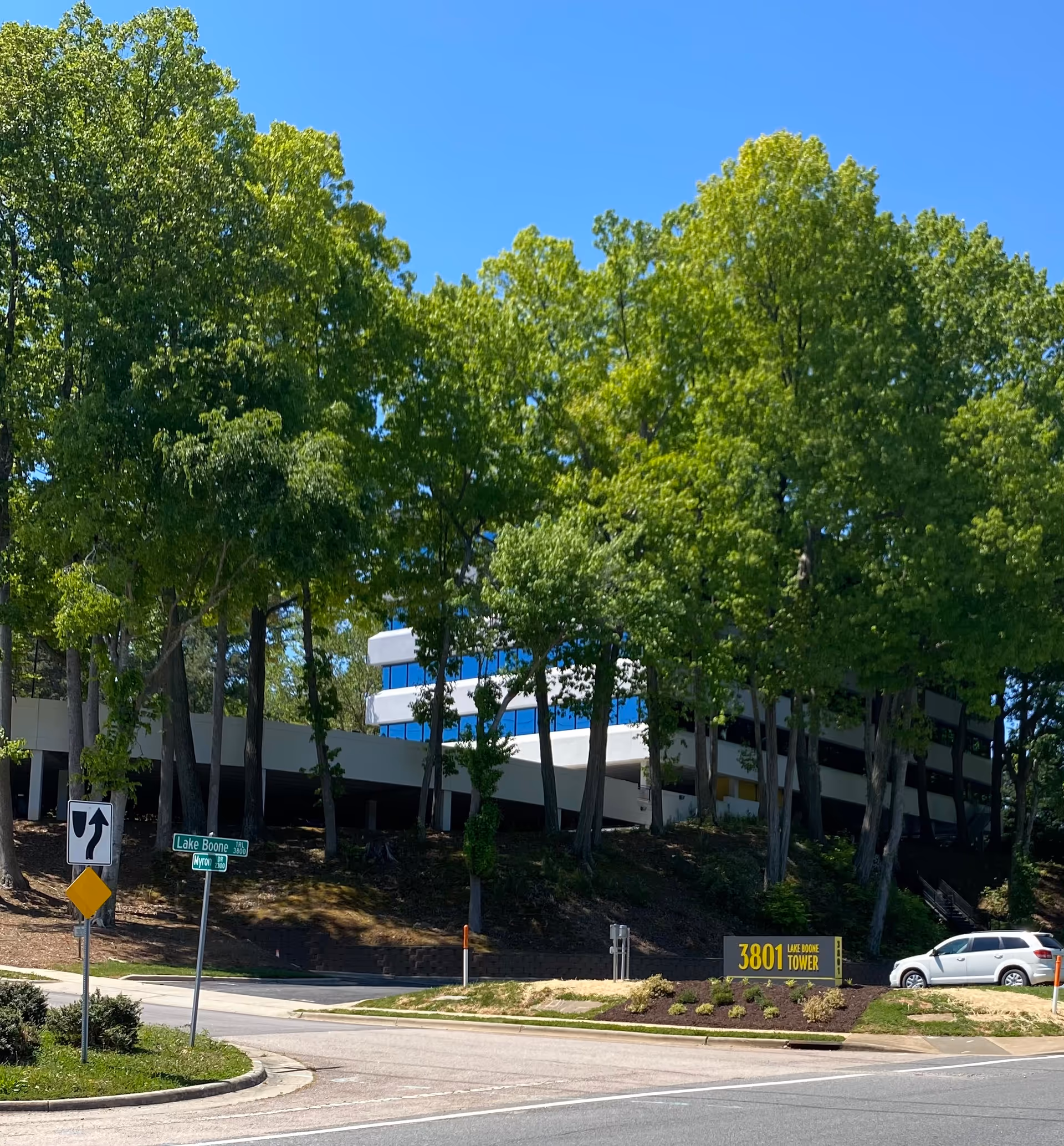 Exterior view of a modern facility partially obscured by tall trees along a road