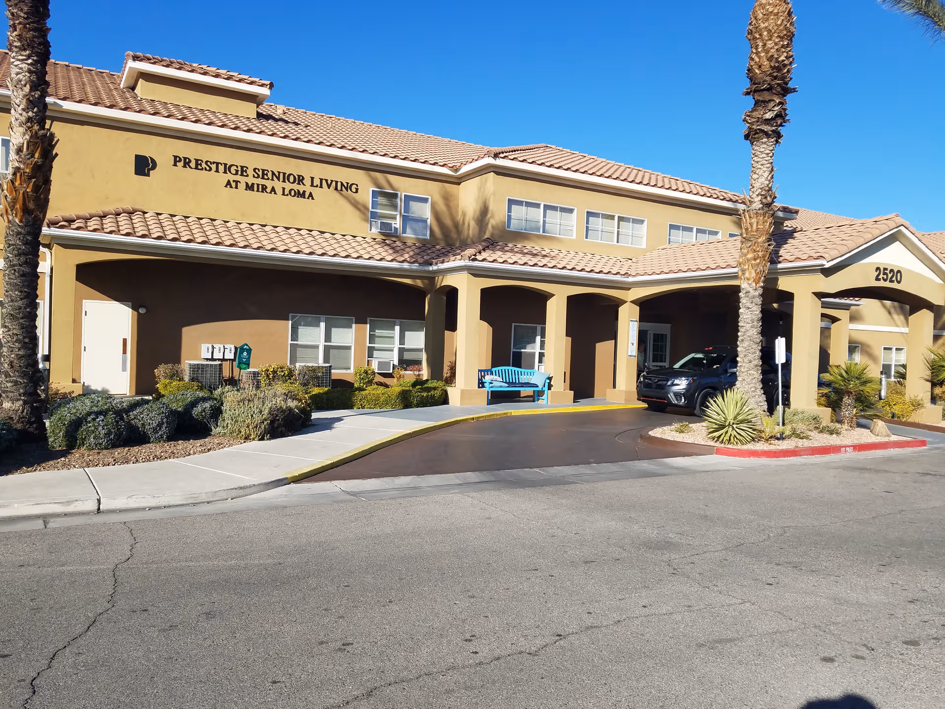 Exterior view of a senior living facility with a covered entrance and palm trees.