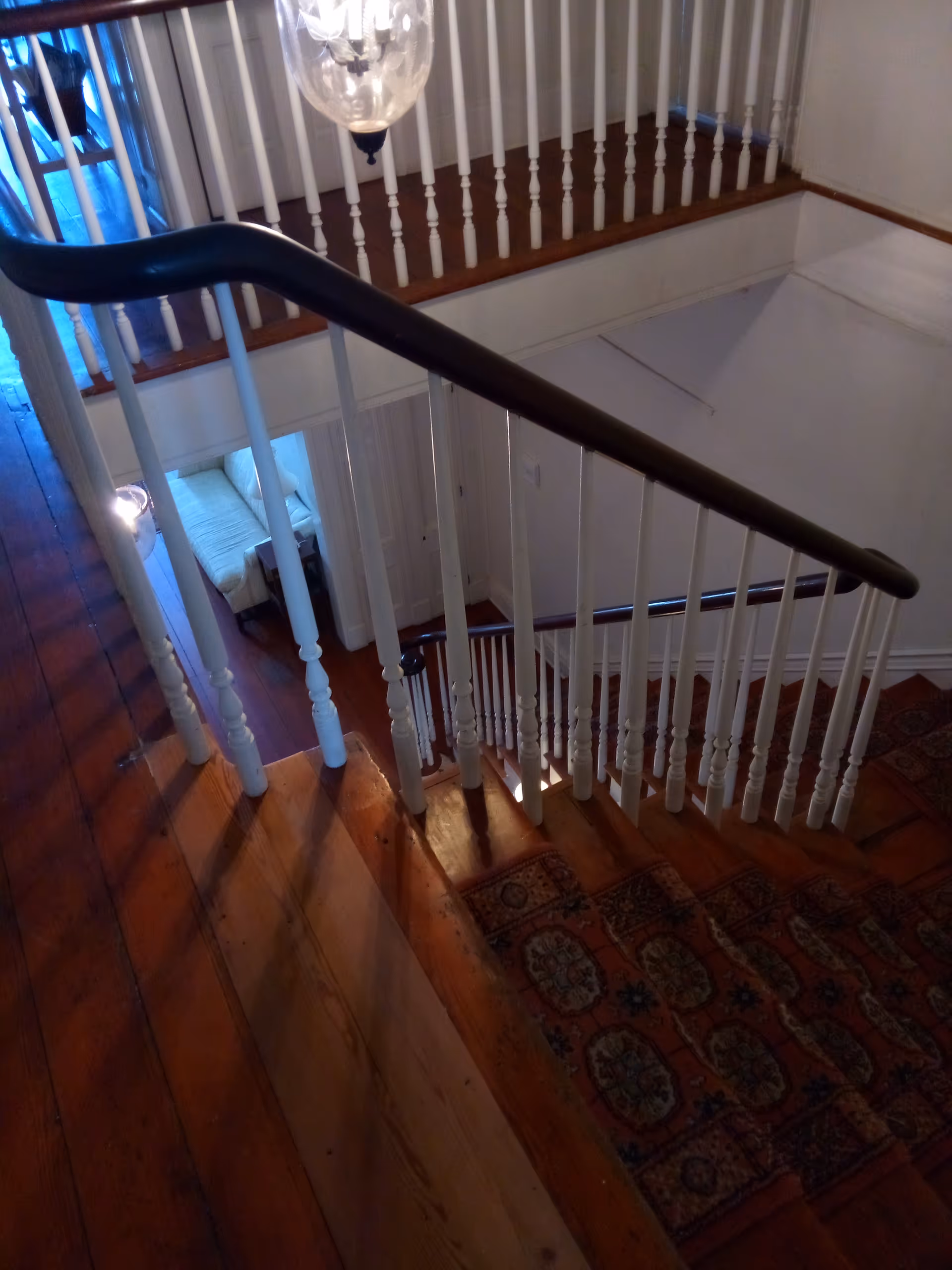 Interior staircase with white balusters, wooden handrail, and a patterned runner rug.