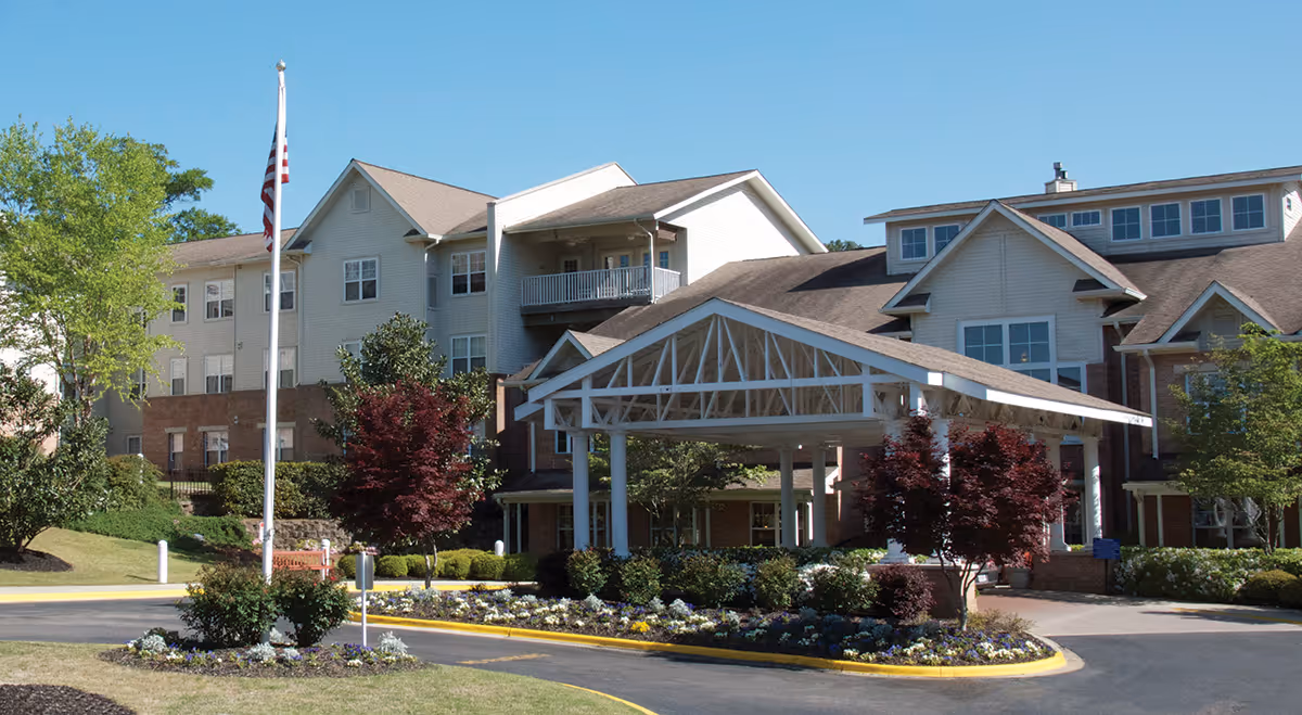 Senior living facility exterior with a covered entrance, landscaped grounds, and flagpole.