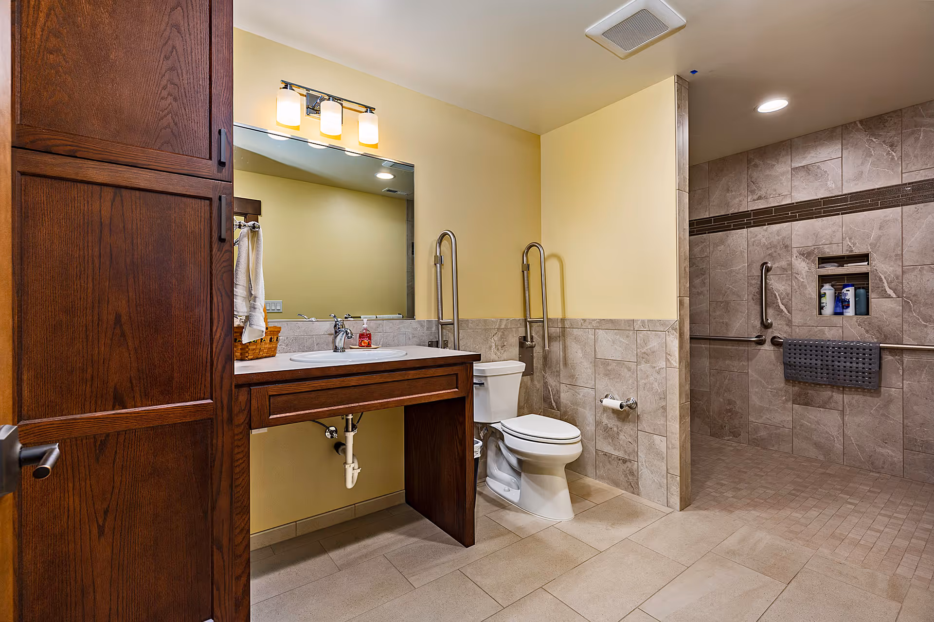 Accessible bathroom with sink vanity, toilet, and spacious walk-in shower in beige tones.