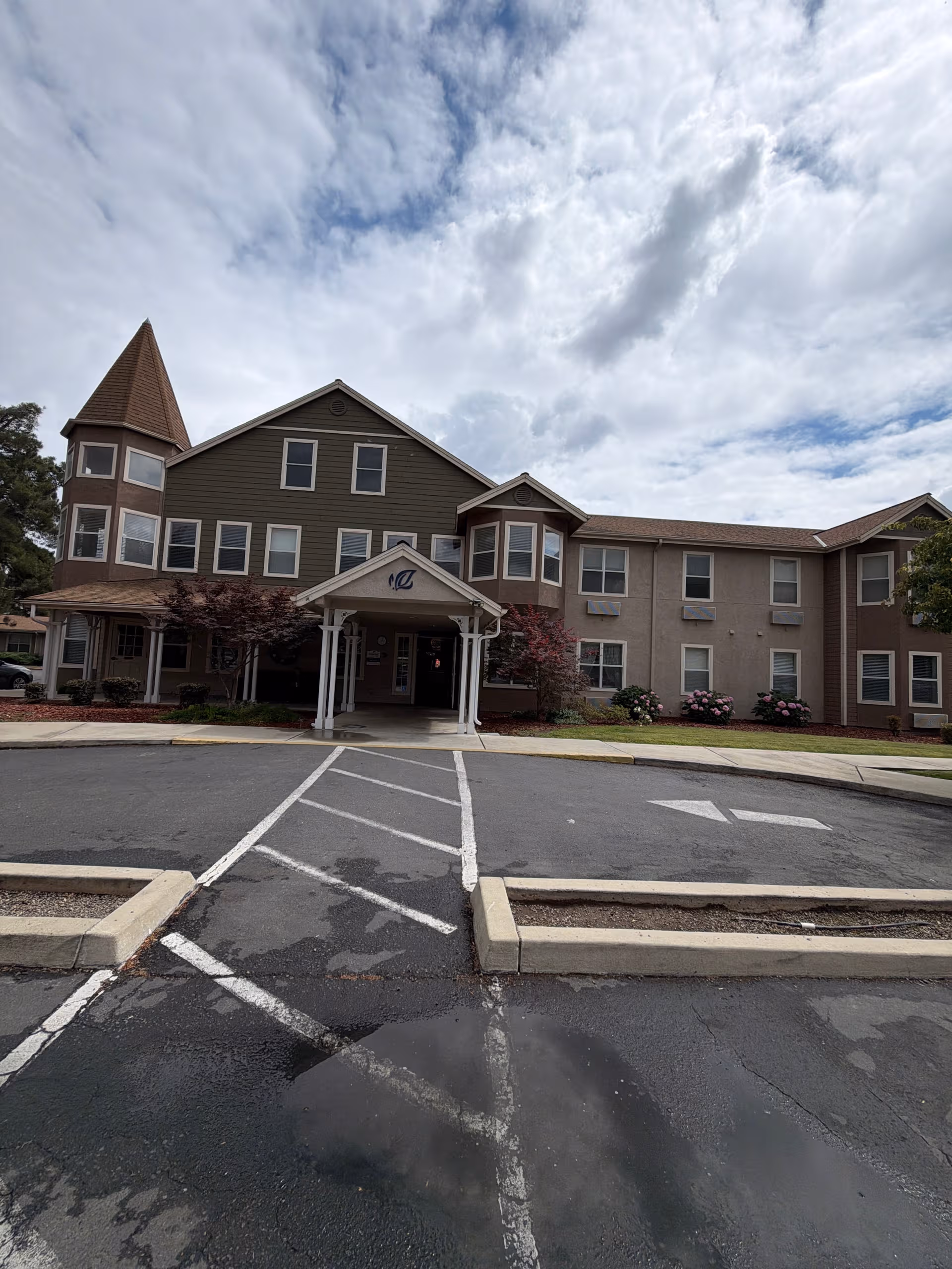 Front view of a multi-story senior living facility with a covered entrance and parking.