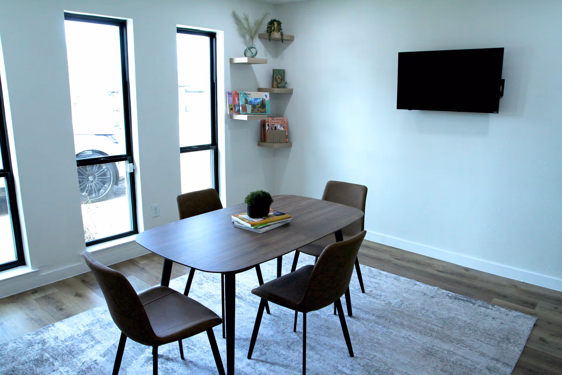 A modern dining area with a table, four chairs, shelves, and a wall-mounted TV.