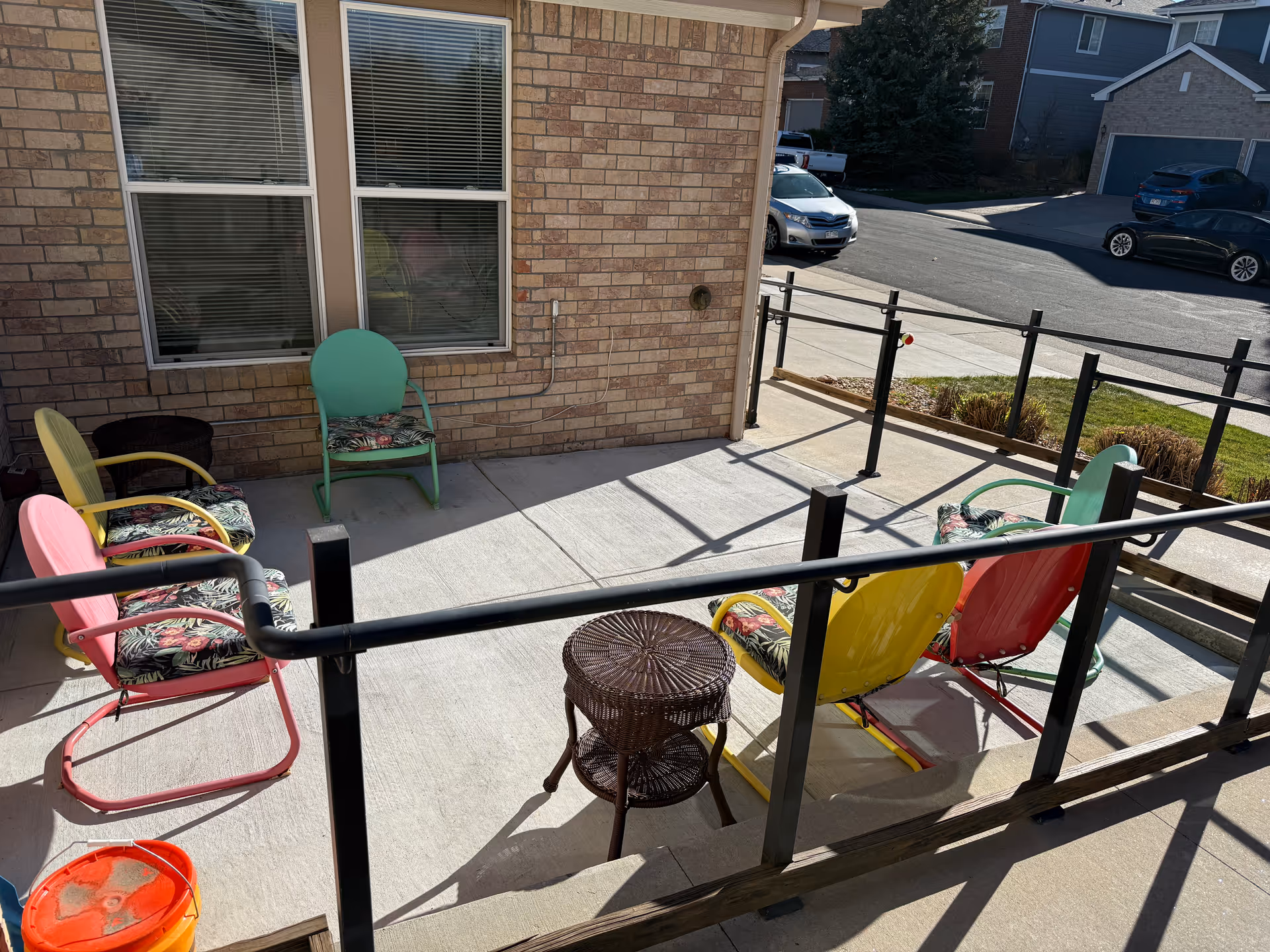 Outdoor patio with colorful chairs and a wicker table beside a brick building.