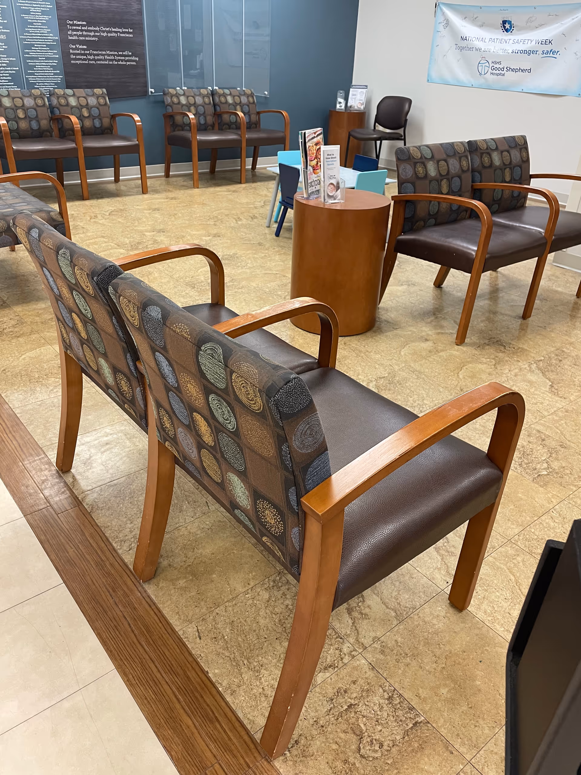 A hospital-style waiting area with patterned chairs, a round table, and brochures.