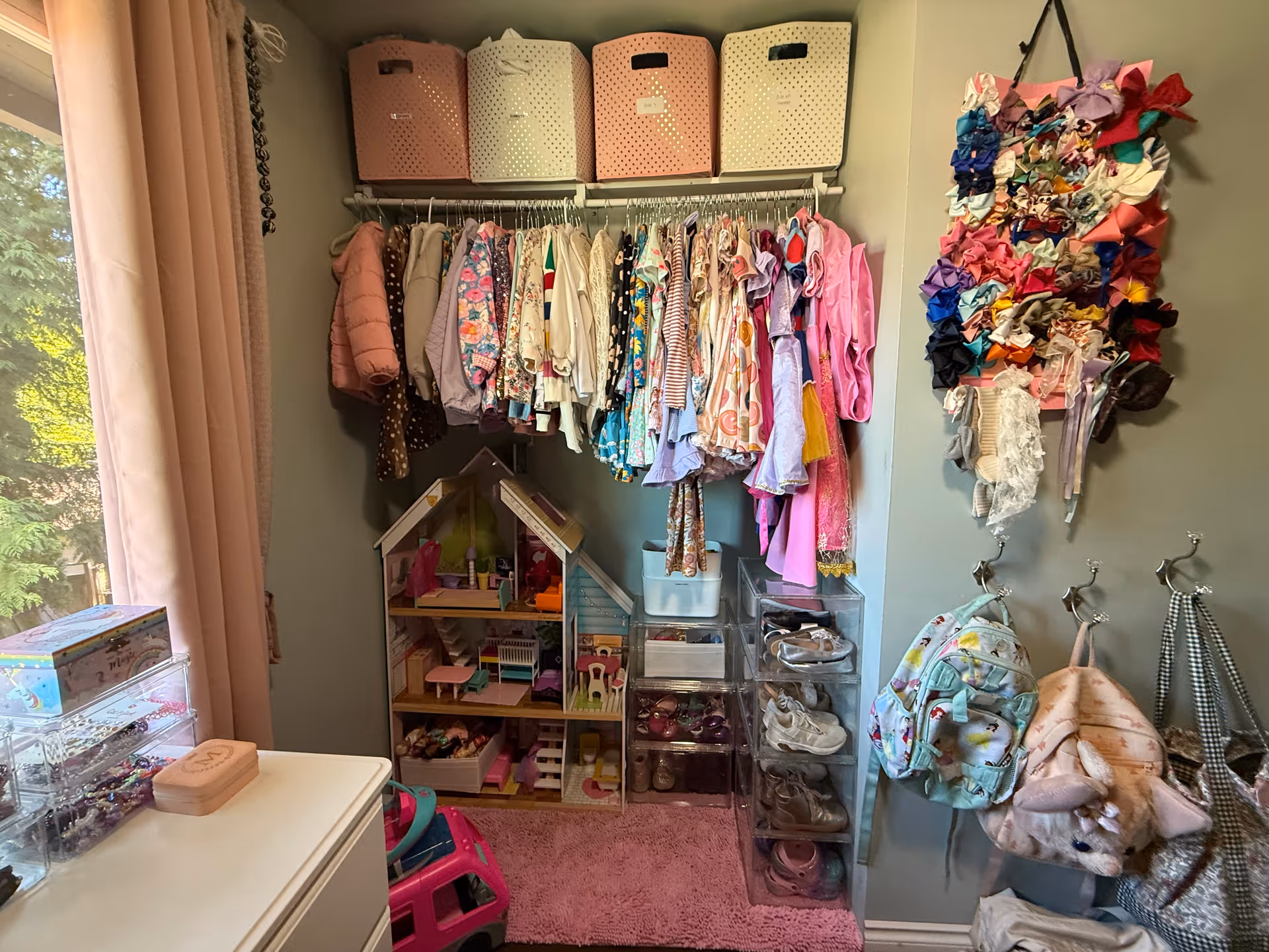 Organized closet with hanging clothes, storage bins, a dollhouse, and toy accessories.