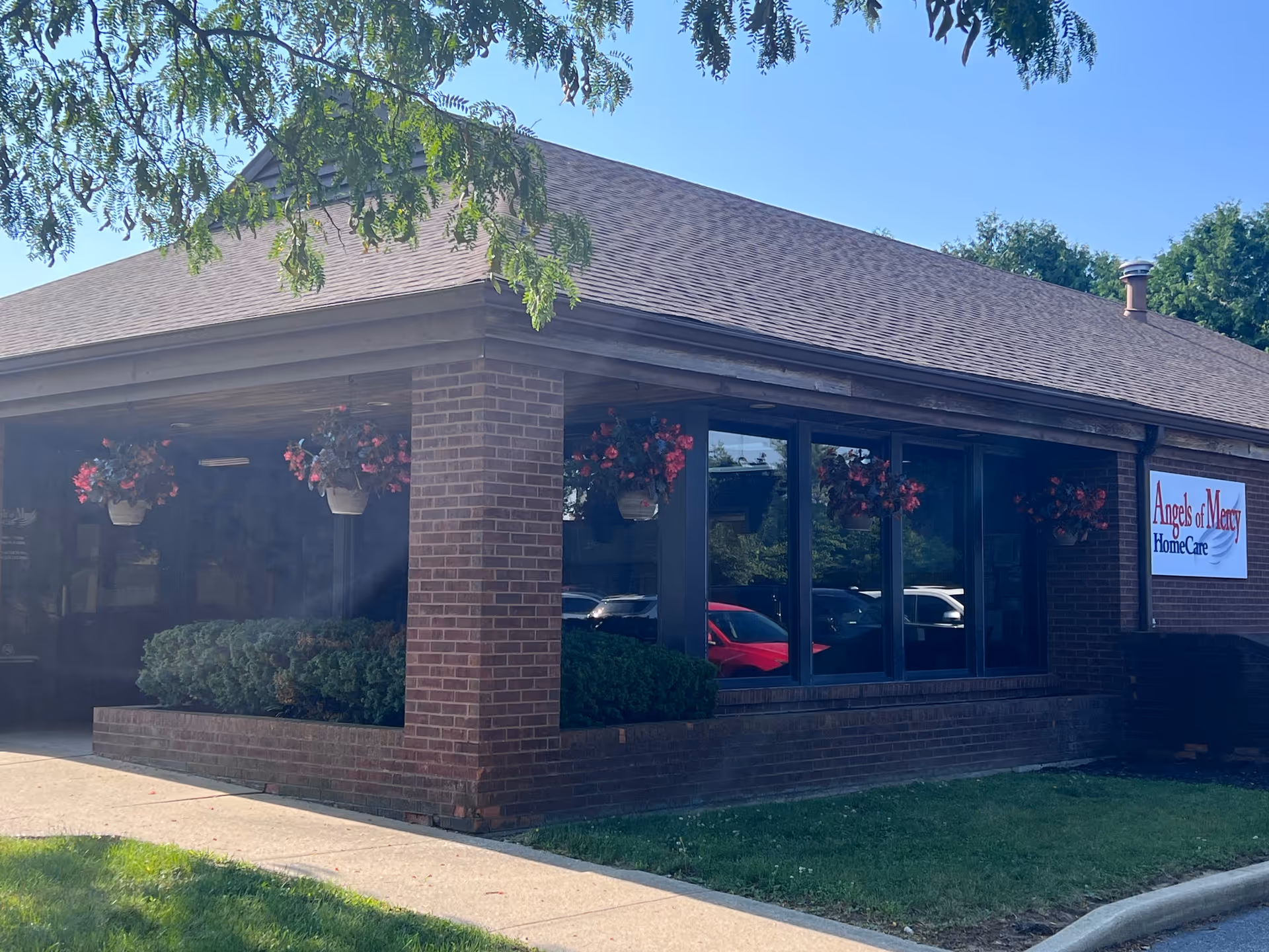 Brick building exterior with large windows, hanging baskets, and Angels of Mercy HomeCare sign.