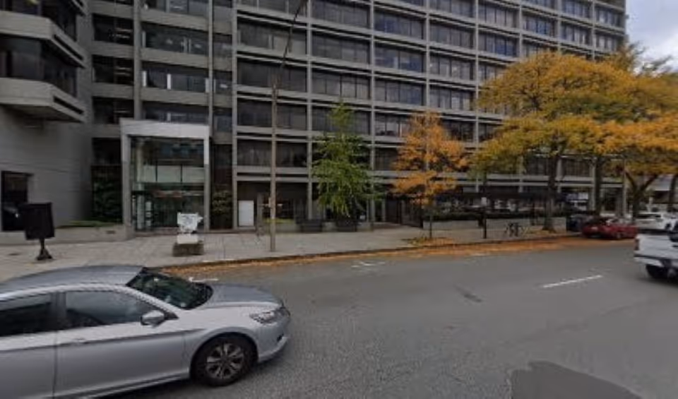 Street view of a modern multi-story building exterior with trees and parked cars.