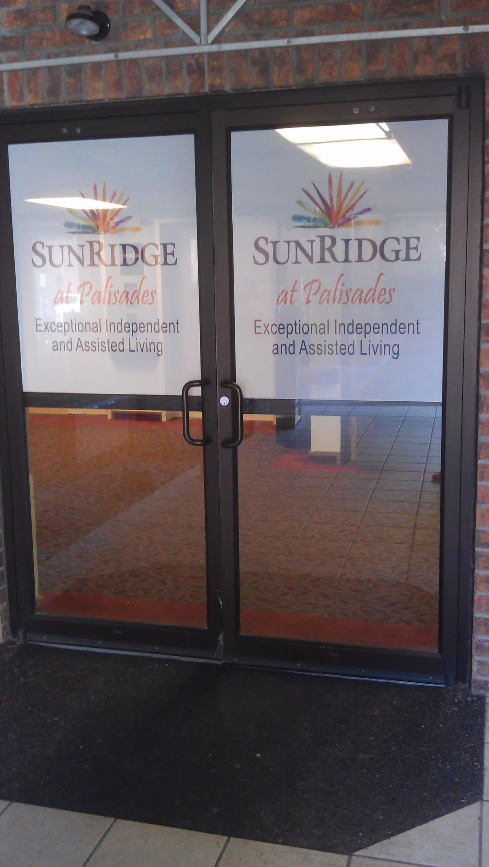 Glass double entrance doors with signage reading 'SunRidge at Palisades Exceptional Independent and Assisted Living.'