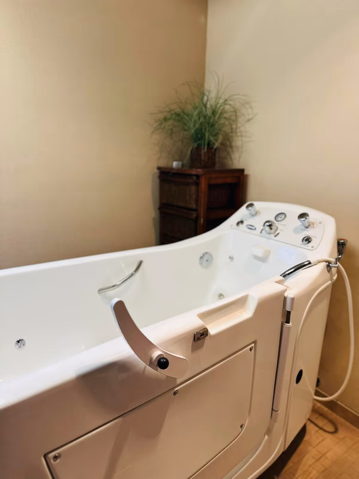 Accessible white walk-in bathtub with safety rail in a beige bathroom