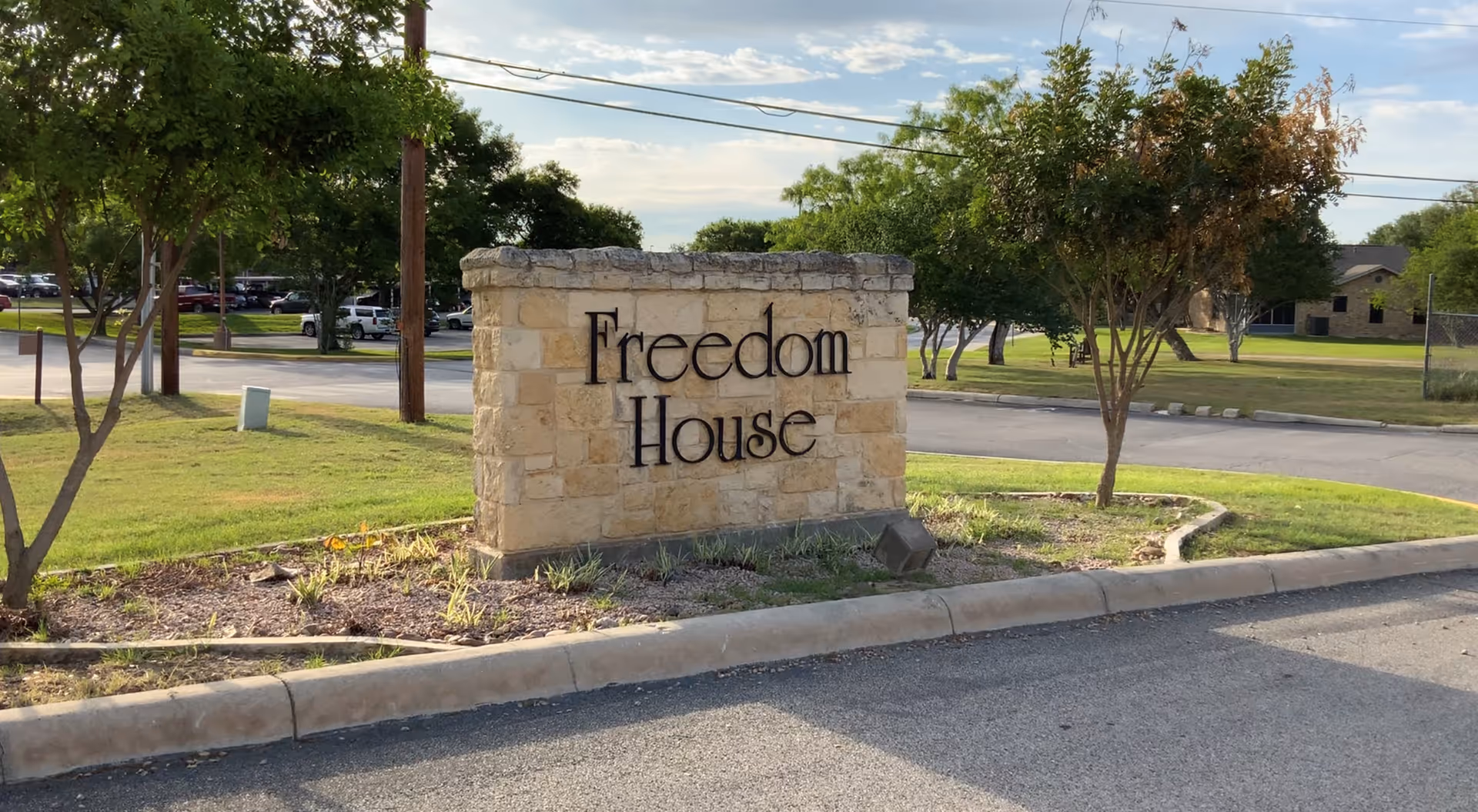 Stone entrance sign reading Freedom House sits in a landscaped front yard.