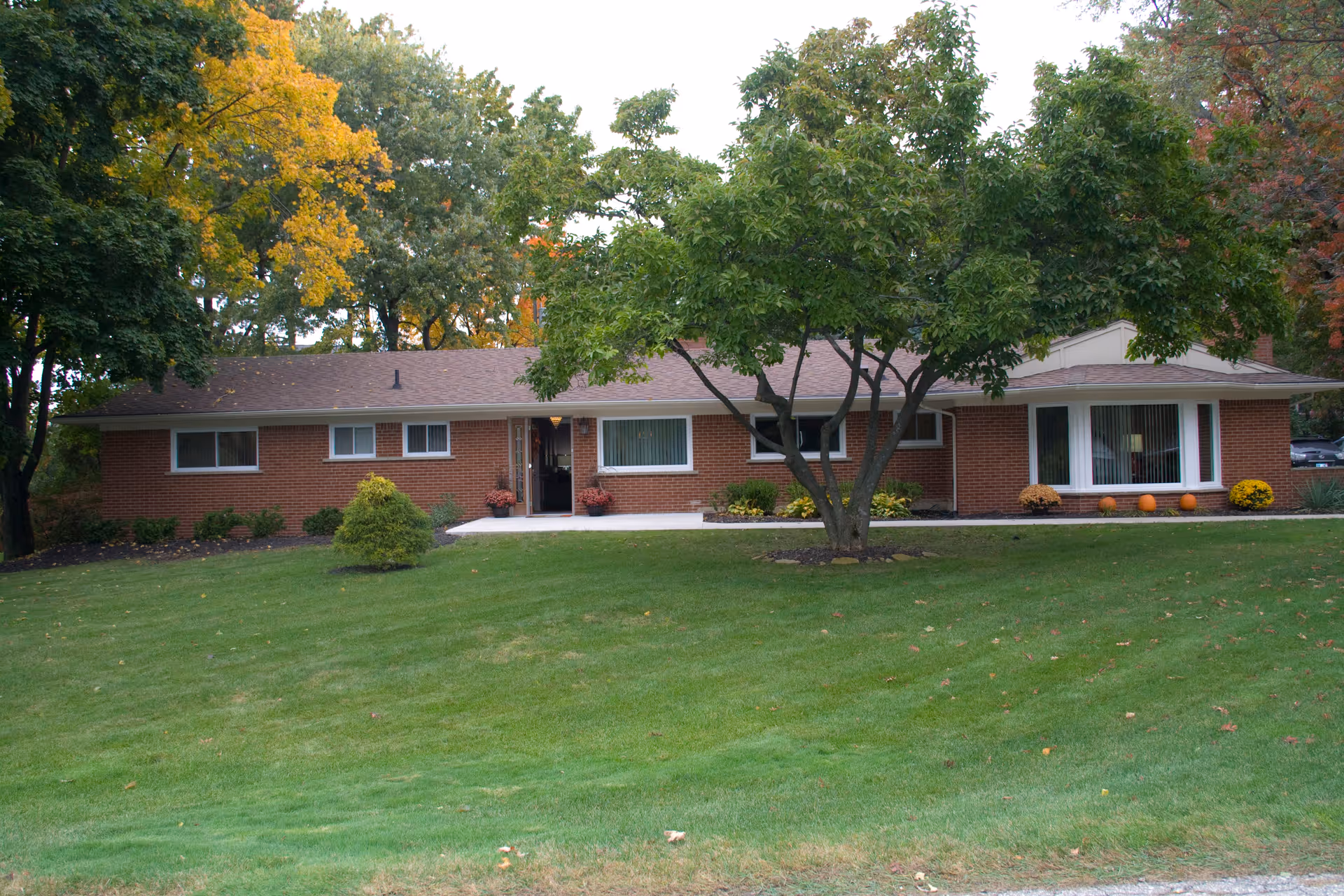A single-story brick senior living facility with a well-kept lawn and mature trees in front