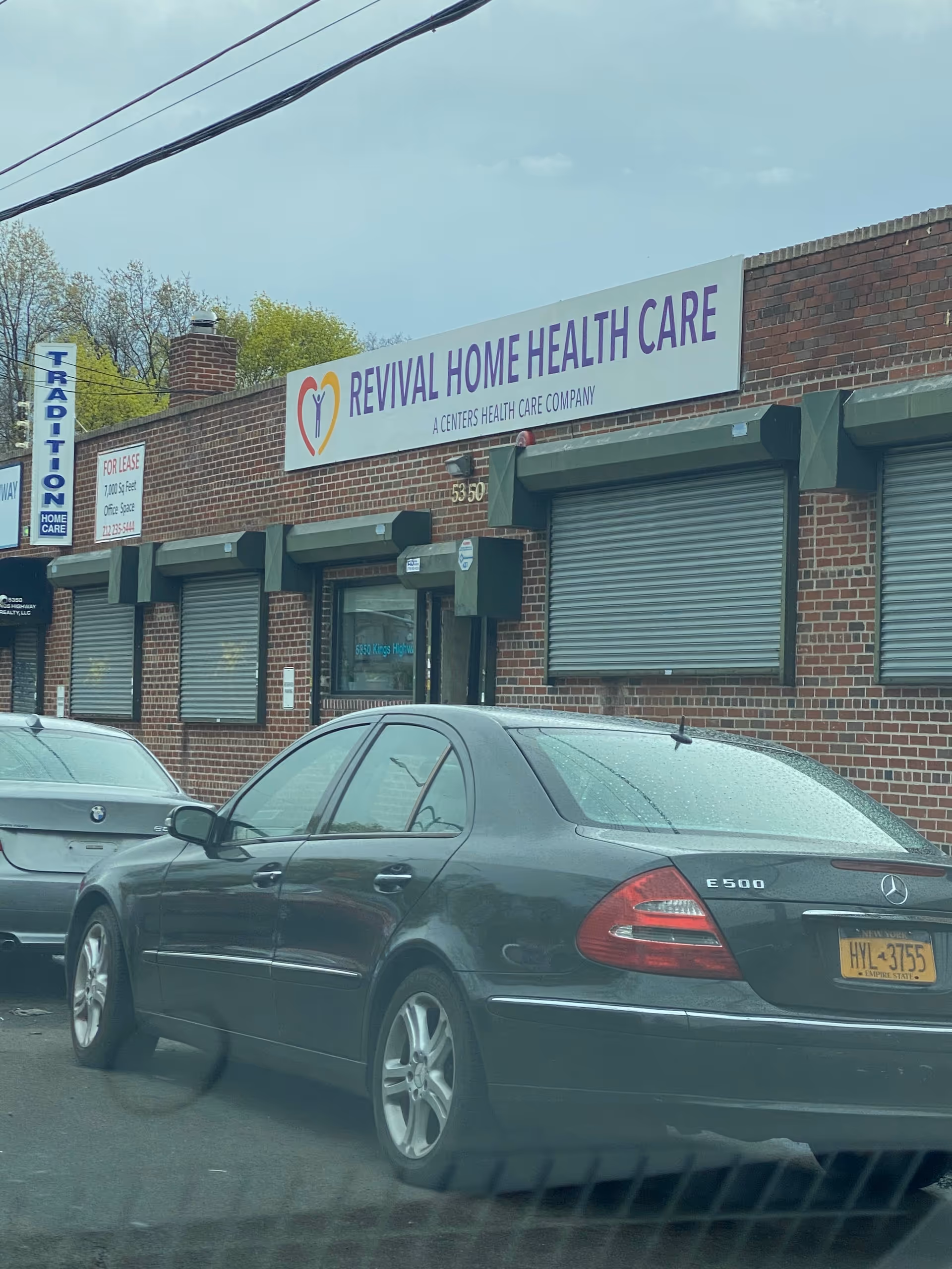 Brick storefront with Revival Home Health Care sign; cars parked along a street.