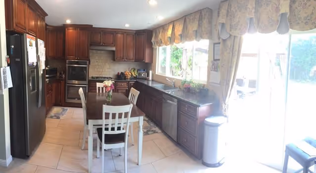 Spacious kitchen with dark wood cabinets, stainless appliances, and a central dining table.